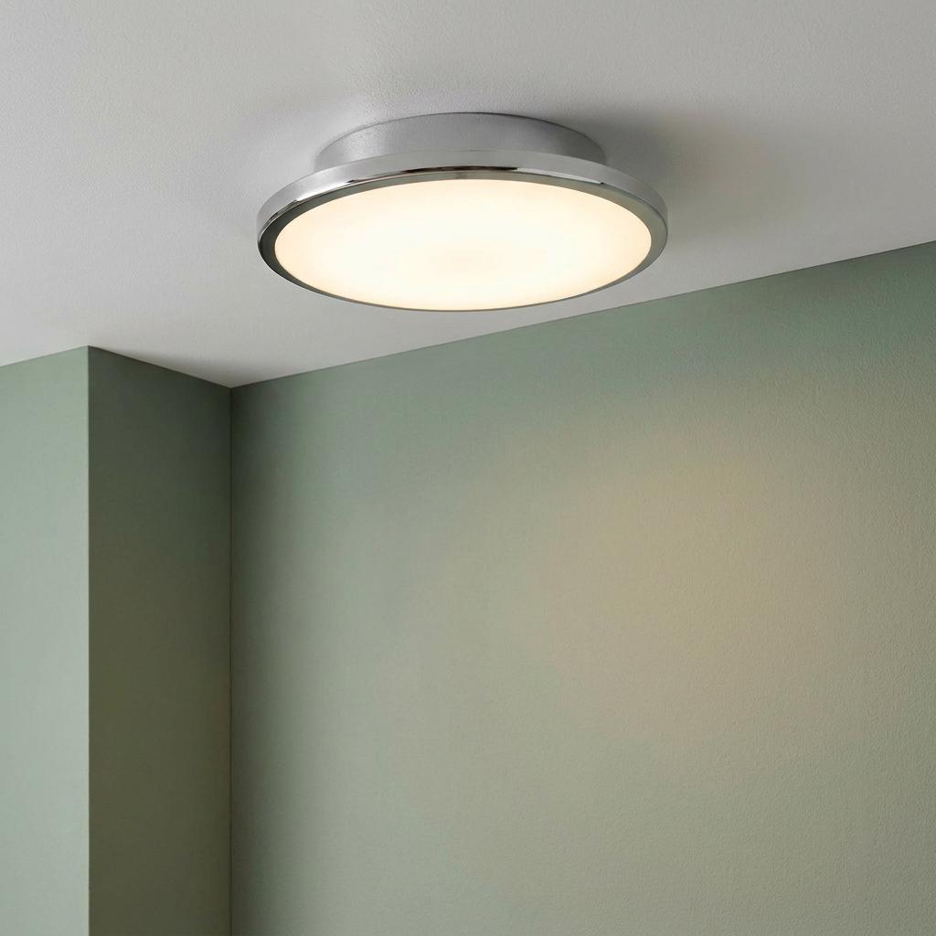 Circular chrome flush ceiling light with a warm glow, mounted on a white ceiling next to a pale green wall.