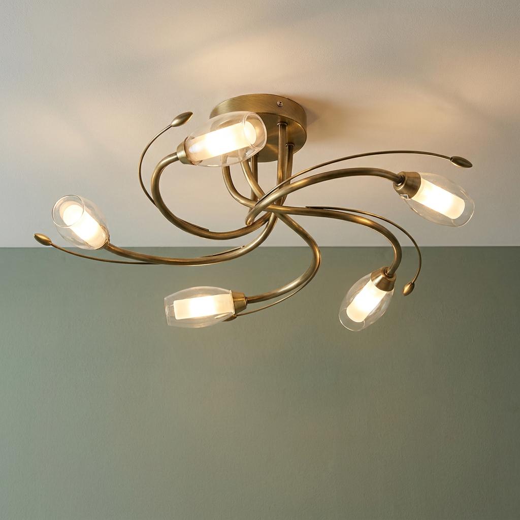 Antique brass ceiling light with five swirling arms and glowing glass capsule shades against a sage green wall.