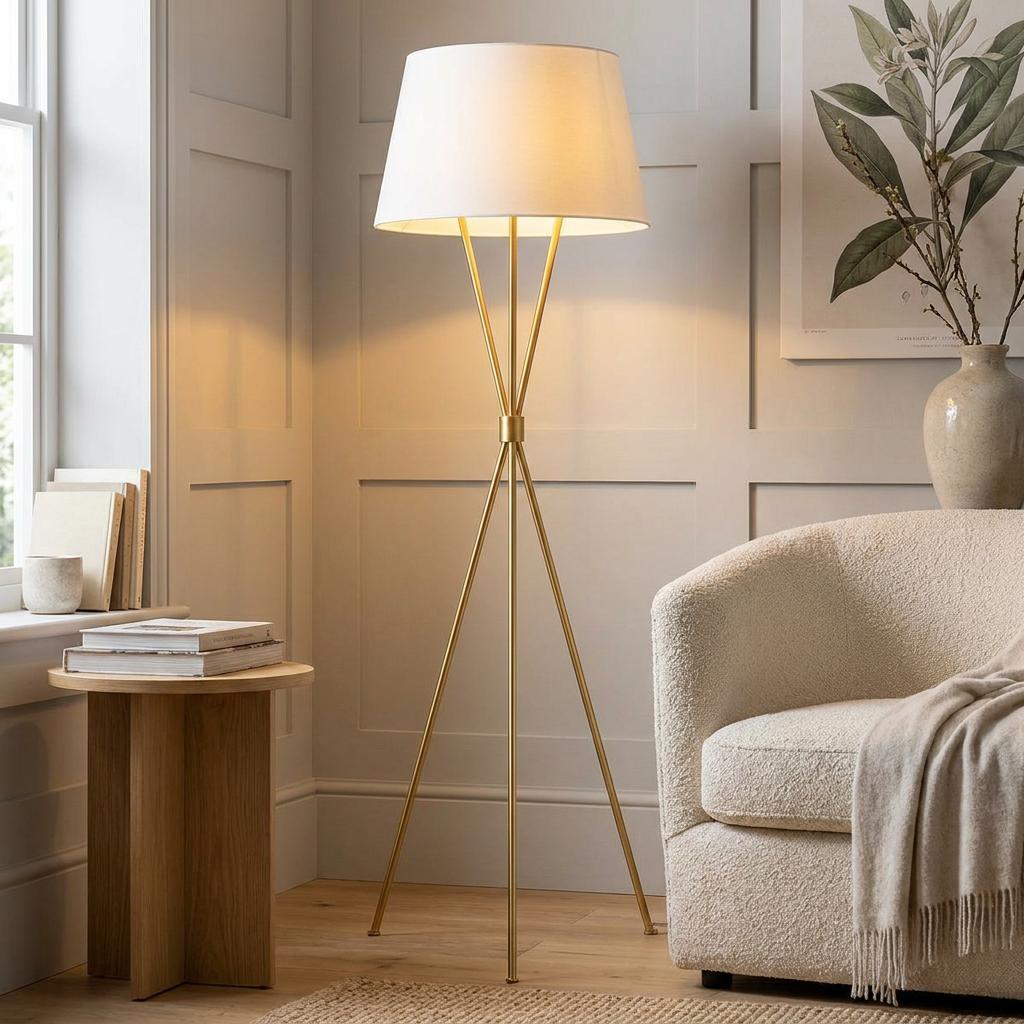 A brass tripod floor lamp with a white tapered drum shade stands in a cozy living room corner.