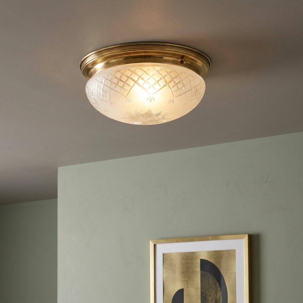 Art Deco flush ceiling light with a cut frosted glass dome and brass base, glowing against a neutral ceiling.