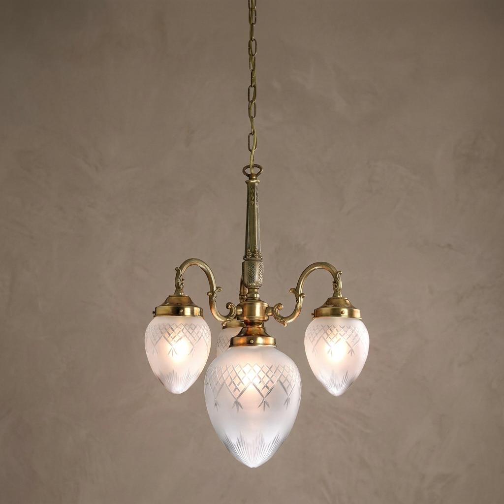 Art Deco brass chandelier with three etched frosted glass shades hanging against a neutral textured wall.
