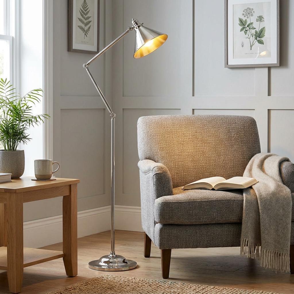 Polished nickel floor lamp with an adjustable arm illuminating a grey armchair in a cozy living room.