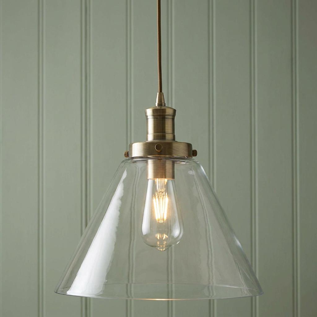 Pyramid 1 light brass ceiling pendant with a clear glass shade and Edison bulb against green wood paneling.