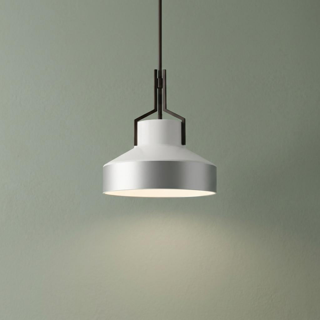 Modern white and silver pendant light glowing against a sage green wall.