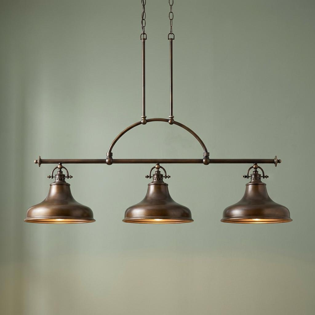A three-light bronze island pendant with metal bell shades and an arched bar, hanging against a neutral wall.