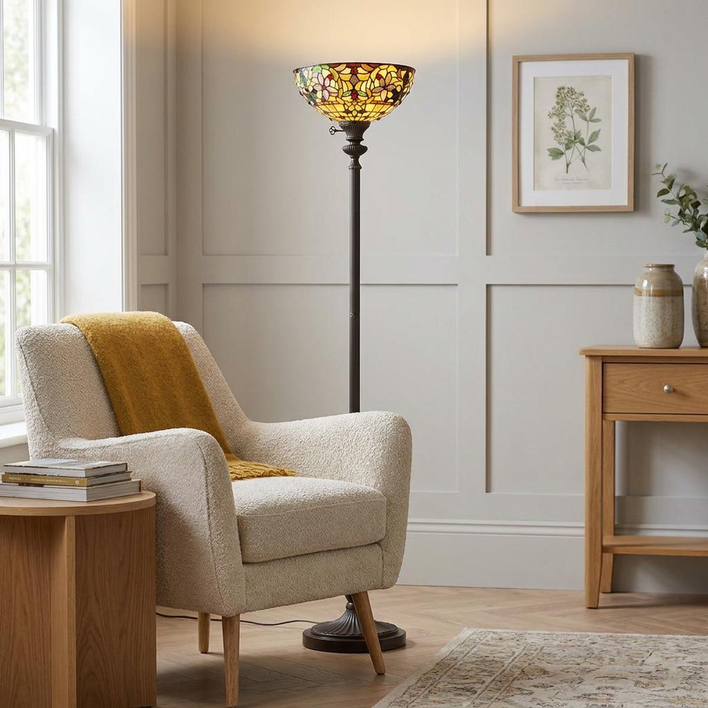 A Quoizel Kami Tiffany floor lamp with a stained glass bowl shade standing beside a cream armchair in a living room.
