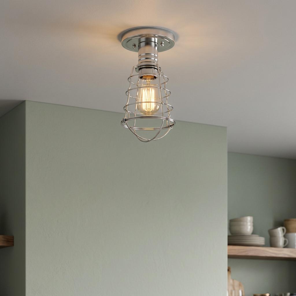 Industrial chrome wire cage semi-flush mount light with a glowing bulb against a light green wall.