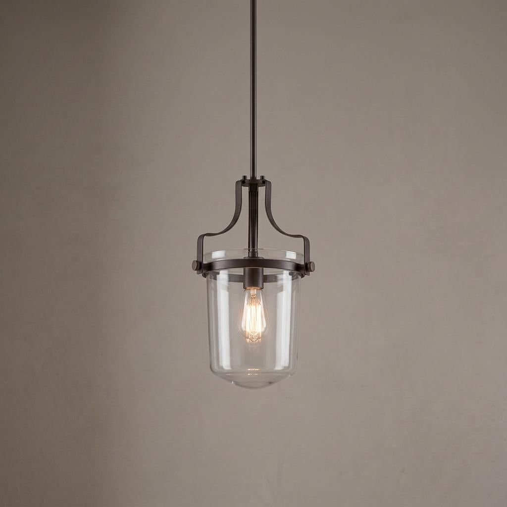 Bronze pendant light with a clear glass jar shade and an exposed vintage bulb against a neutral wall.
