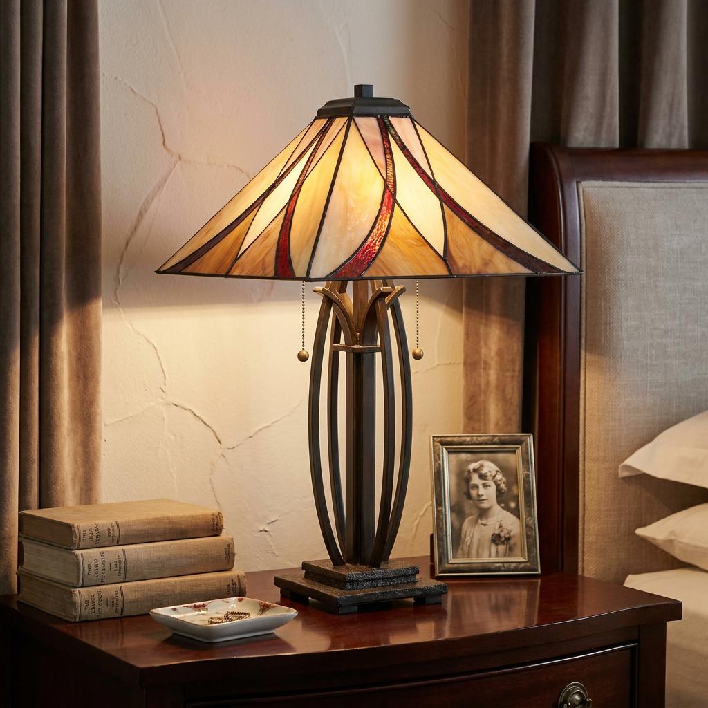 Tiffany-style table lamp with a geometric amber and red glass shade on a bronze base, sitting on a bedside table.