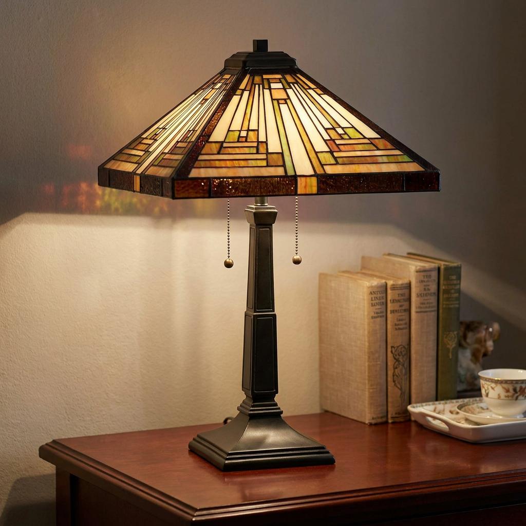 Mission-style Tiffany table lamp with a geometric stained glass shade on a wooden desk next to vintage books.