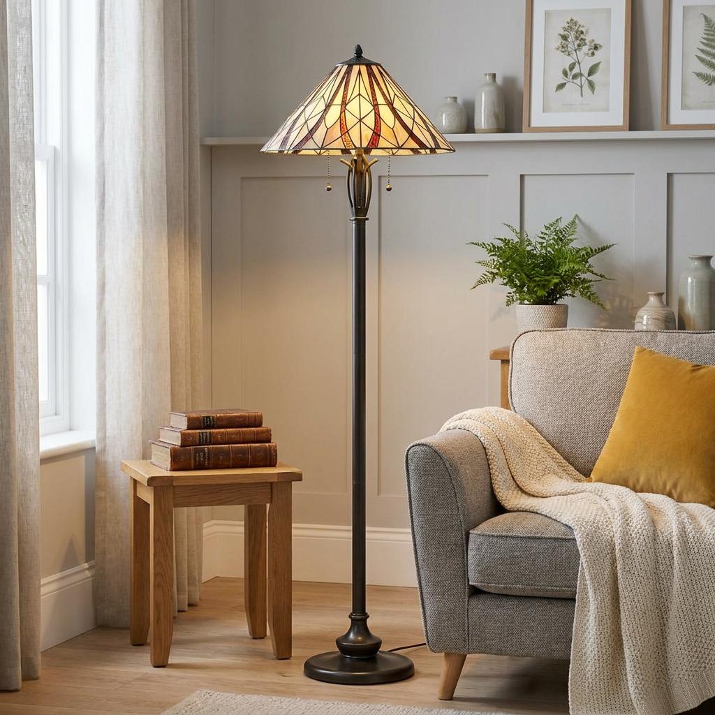 Quoizel Victory Tiffany floor lamp with a stained glass shade lit in a cozy living room beside a grey armchair.