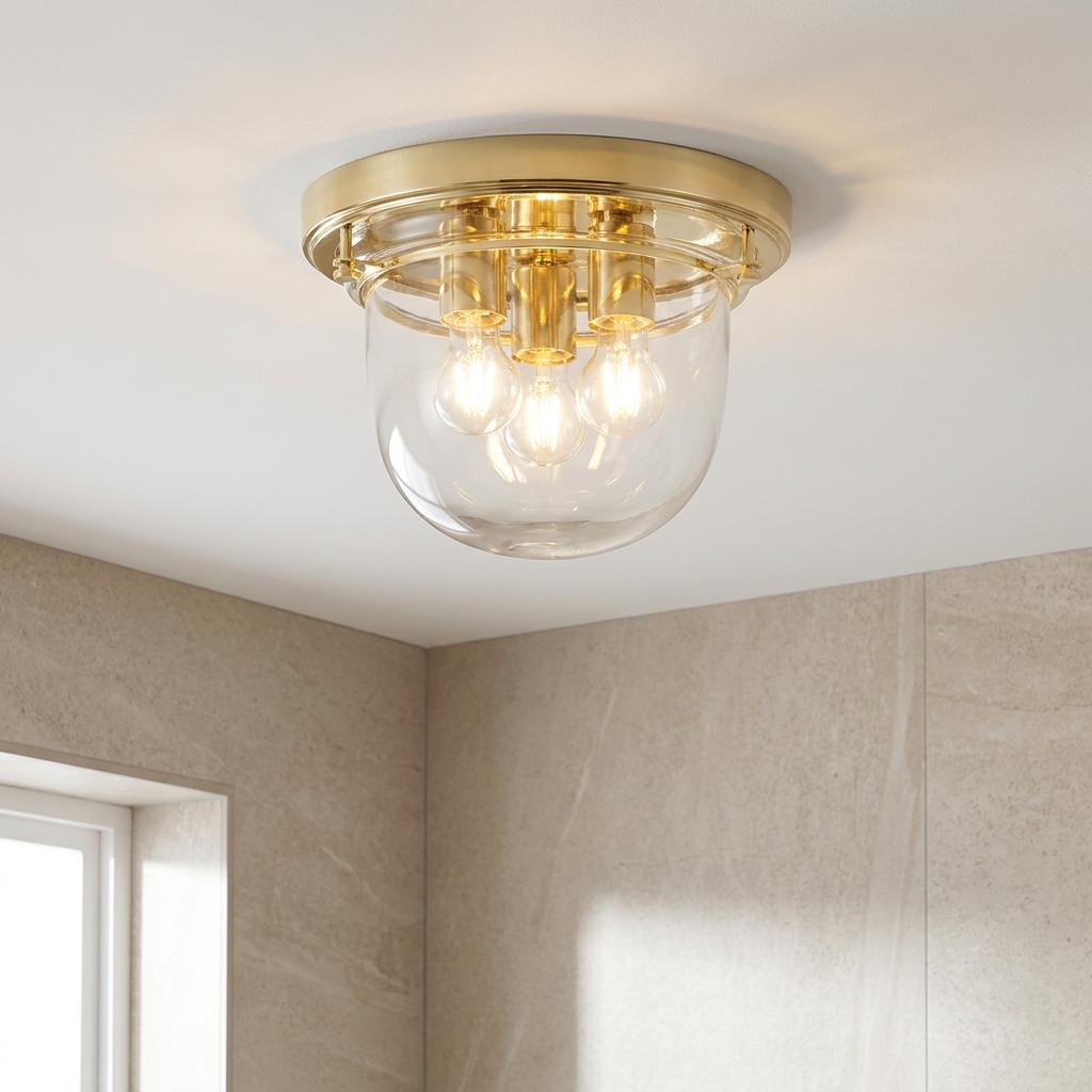 Polished brass 3-light bathroom flush mount with clear glass bowl shade on a light-colored ceiling.
