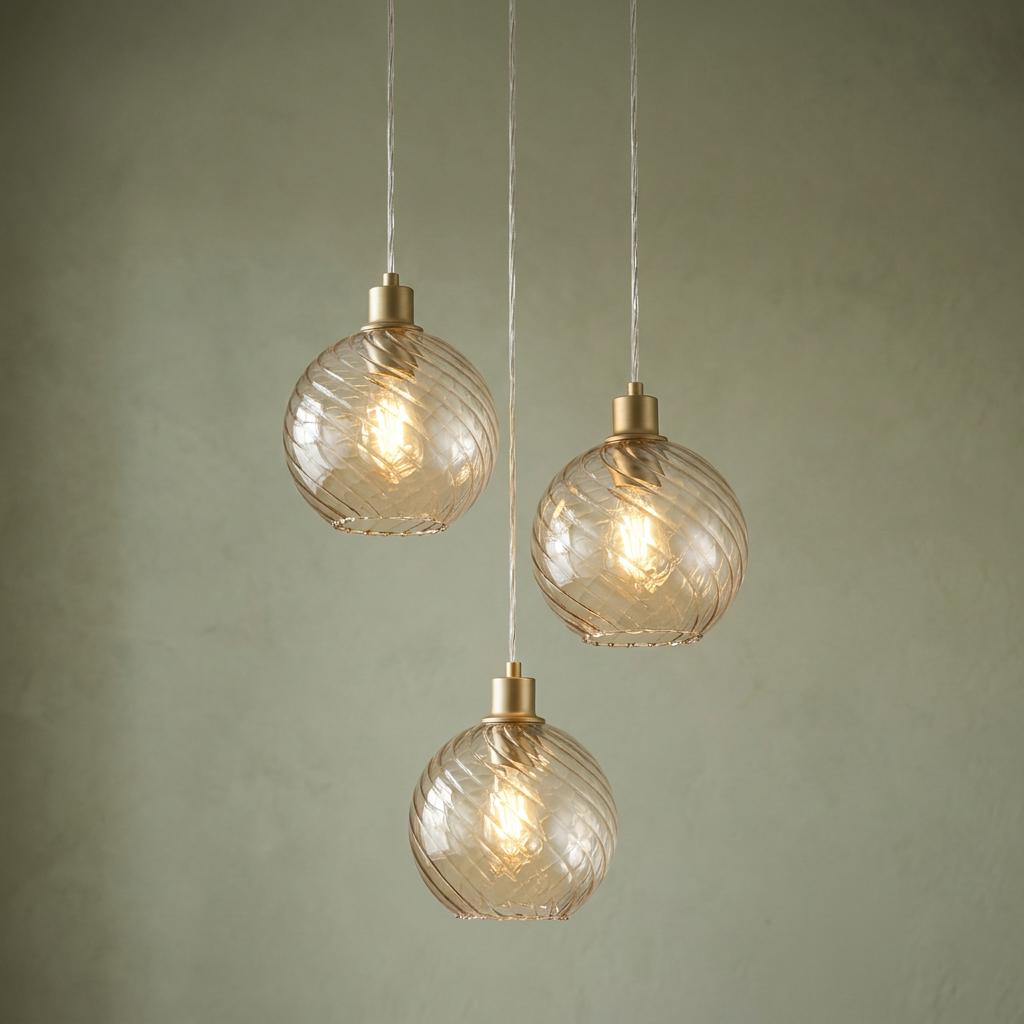 Three gold ceiling pendants with swirl-textured champagne glass globes glowing against a green wall.