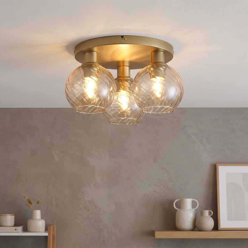 A three-light gold and champagne ceiling fixture with swirl glass globes illuminated against a gray wall.