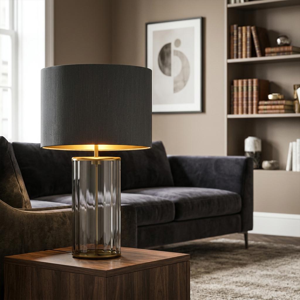 Reno smoked glass and aged brass table lamp with a black shade on a wooden table in a contemporary living room.