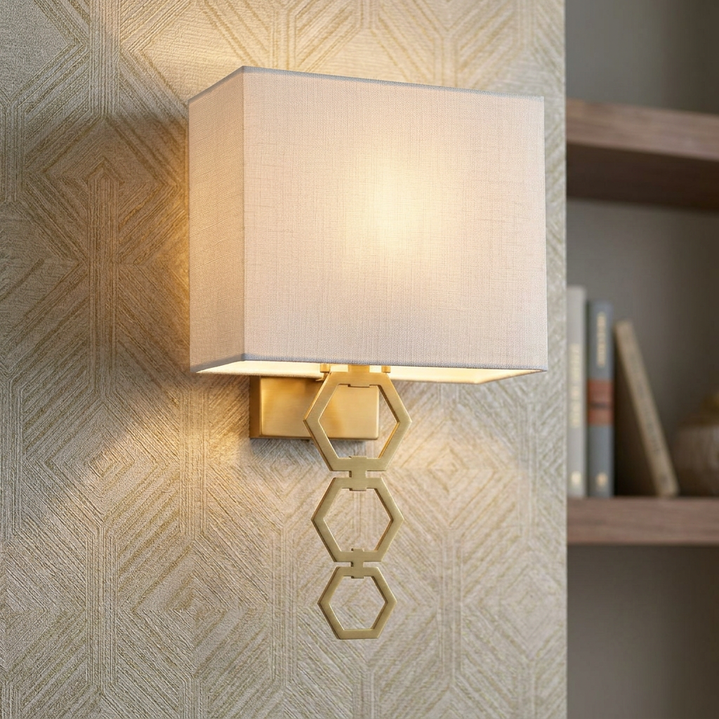 Aged brass wall light with a white fabric shade and three interlocking hexagonal rings on textured wallpaper.