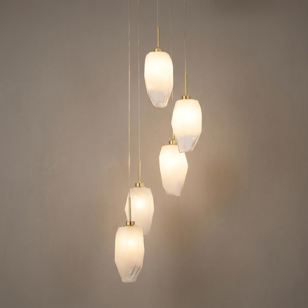 Five-light multi-drop pendant with satin brass fixtures and rocky white glass shades hanging at staggered heights.