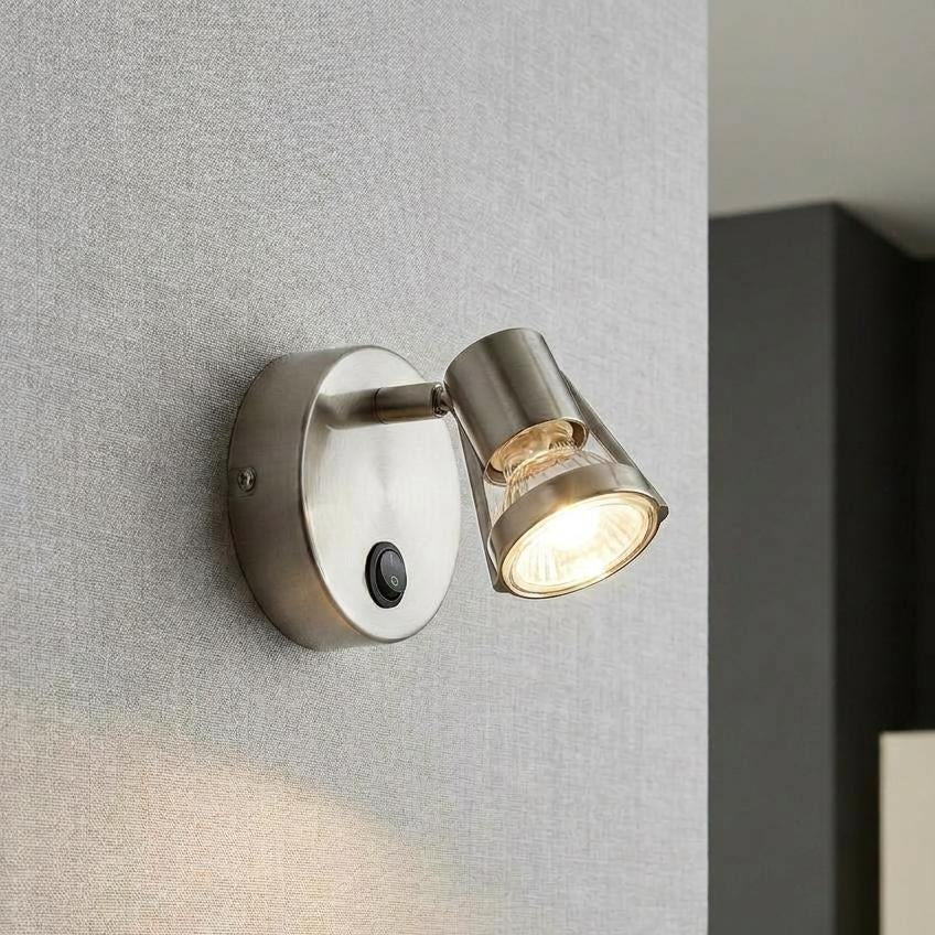 Antique chrome single switched spotlight illuminated on a grey textured wall.