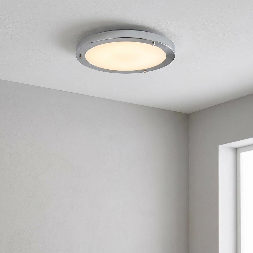 Large chrome flush ceiling light with frosted glass, illuminated on a white ceiling in a bright room.