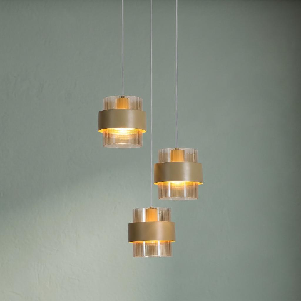 Three staggered pendant lights with amber ribbed glass shades and sand metal bands against a pale green wall.