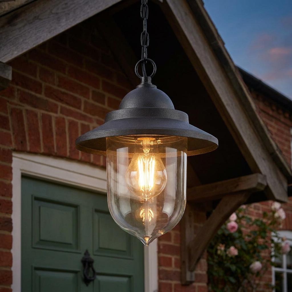 Black outdoor chain lantern with a teardrop glass shade hanging from a wooden porch in front of a brick house.