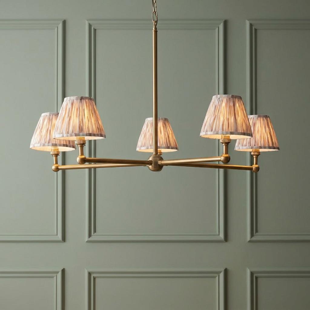 Santiago five-light brass pendant chandelier with neutral ikat pleated shades against a green paneled wall.