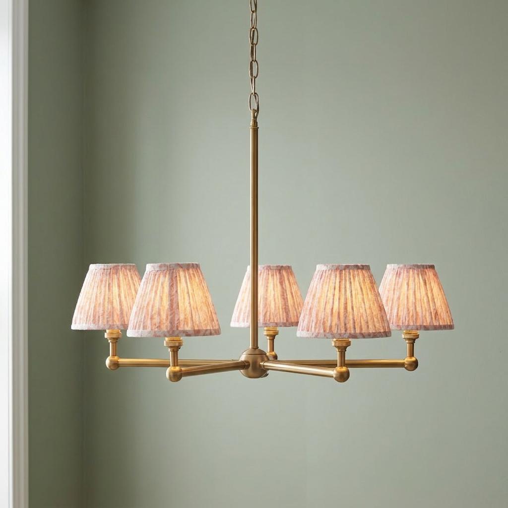 Five-light brass pendant chandelier with peachy pleated leaf-patterned shades against a sage green wall.