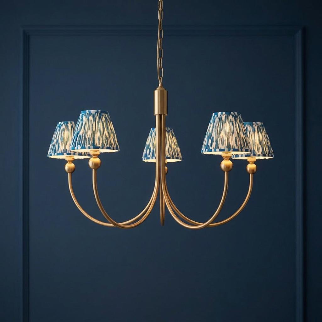 Five-arm brass chandelier featuring blue ikat patterned lampshades set against a dark blue paneled wall.