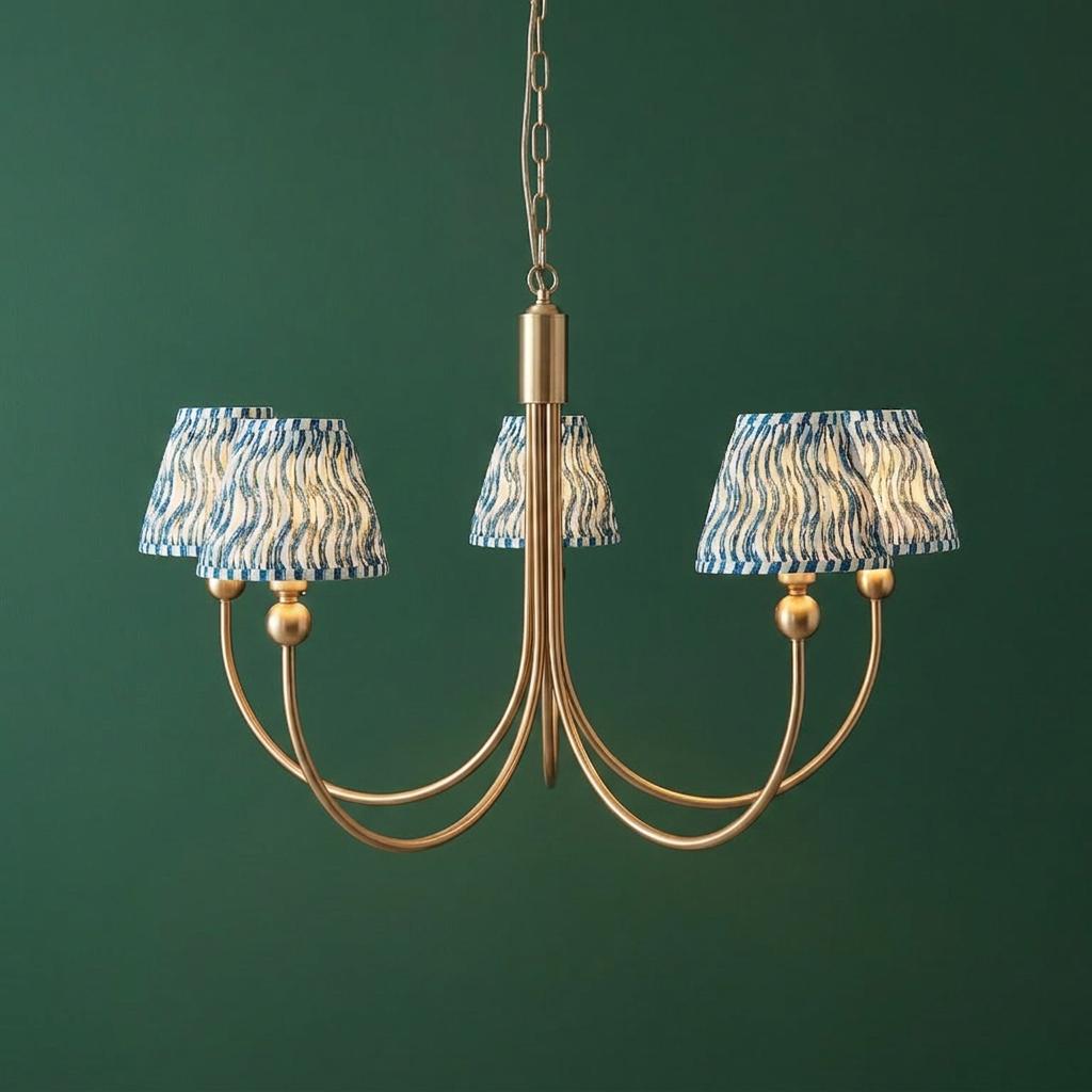 Five-arm brass chandelier with blue ripple patterned shades against a dark green wall.