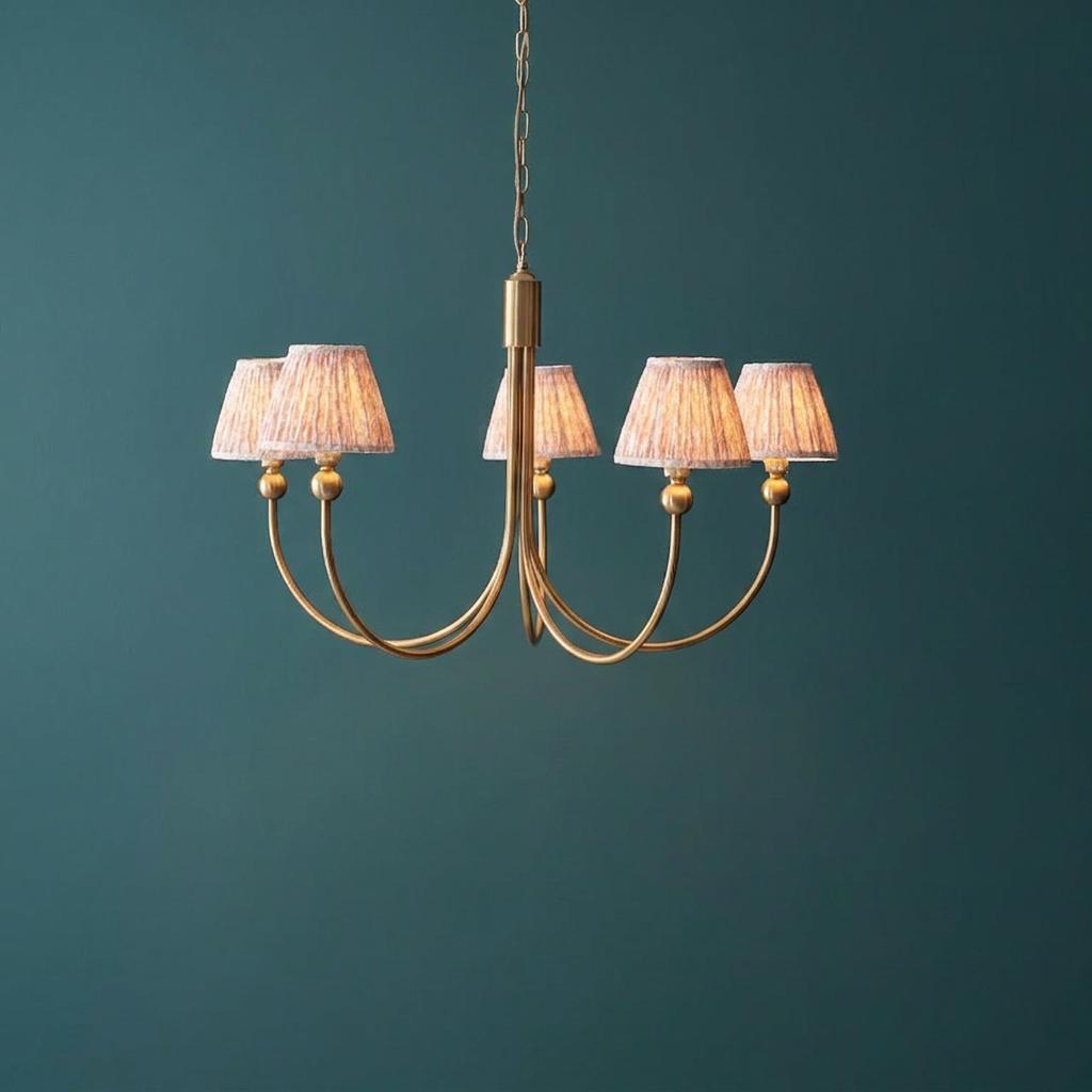 Five-arm brass chandelier with pleated peachy leaf shades against a dark teal background.
