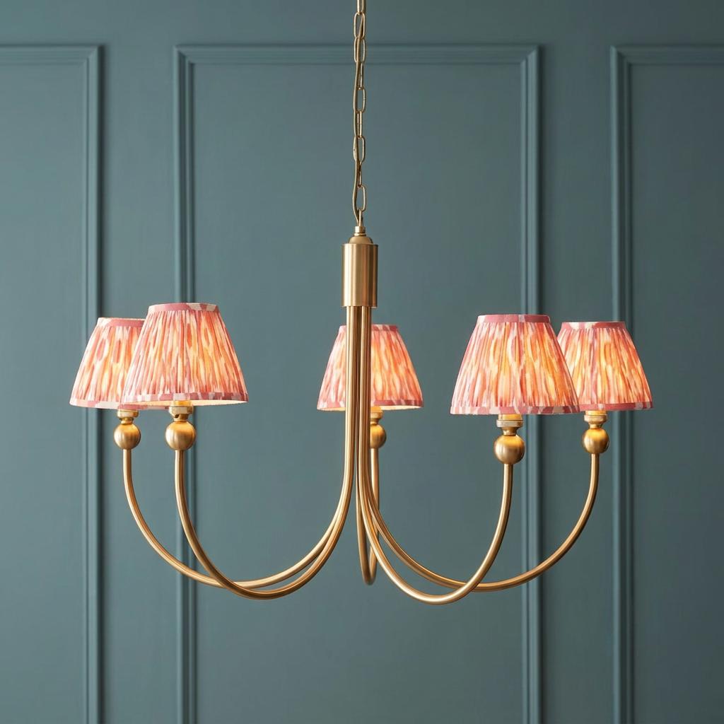 Santiago brass chandelier with pink ikat shades on five curved arms, hanging against a teal paneled wall.