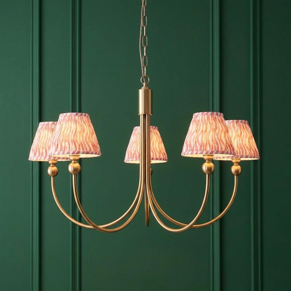 Five-arm brass chandelier with pink ripple patterned lampshades against a dark green paneled wall.