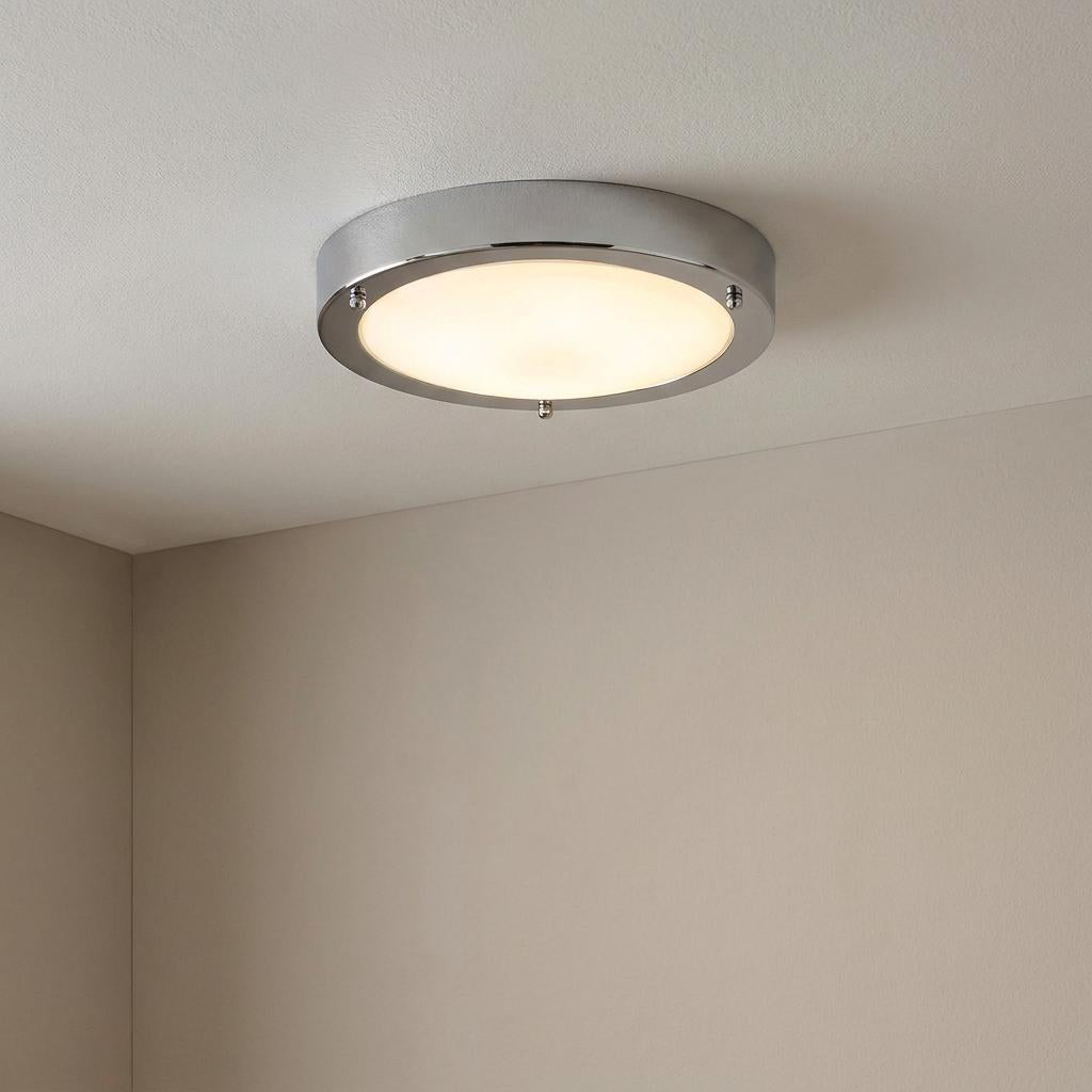 A circular chrome flush ceiling light with frosted glass glowing warmly on a white ceiling.