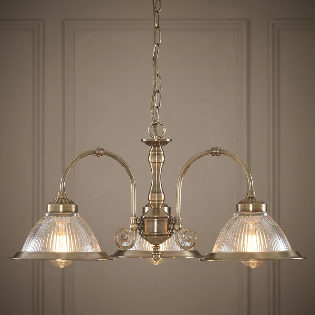 Antique brass 3-light pendant with ribbed glass bowl shades hanging against a paneled wall.