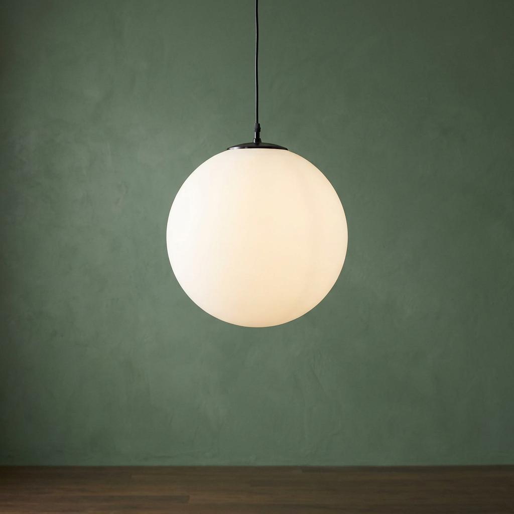 Opal glass sphere pendant light hanging against a textured green wall and wooden flooring.
