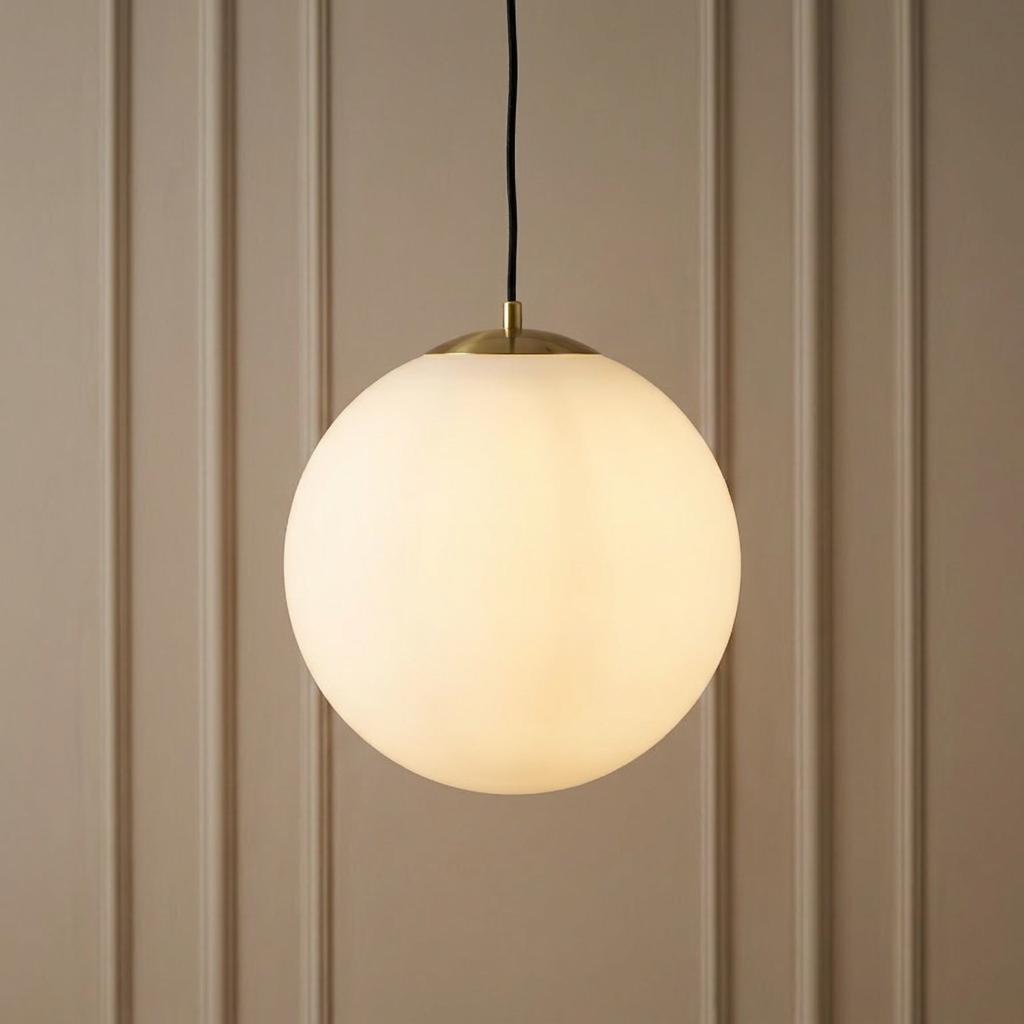 Illuminated opal glass globe pendant light with brass hardware hanging against a neutral panelled wall.