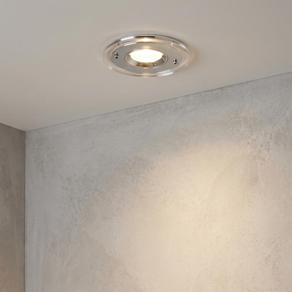 Chrome IP65 bathroom downlight with a clear outer ring casting warm light on a textured grey wall.