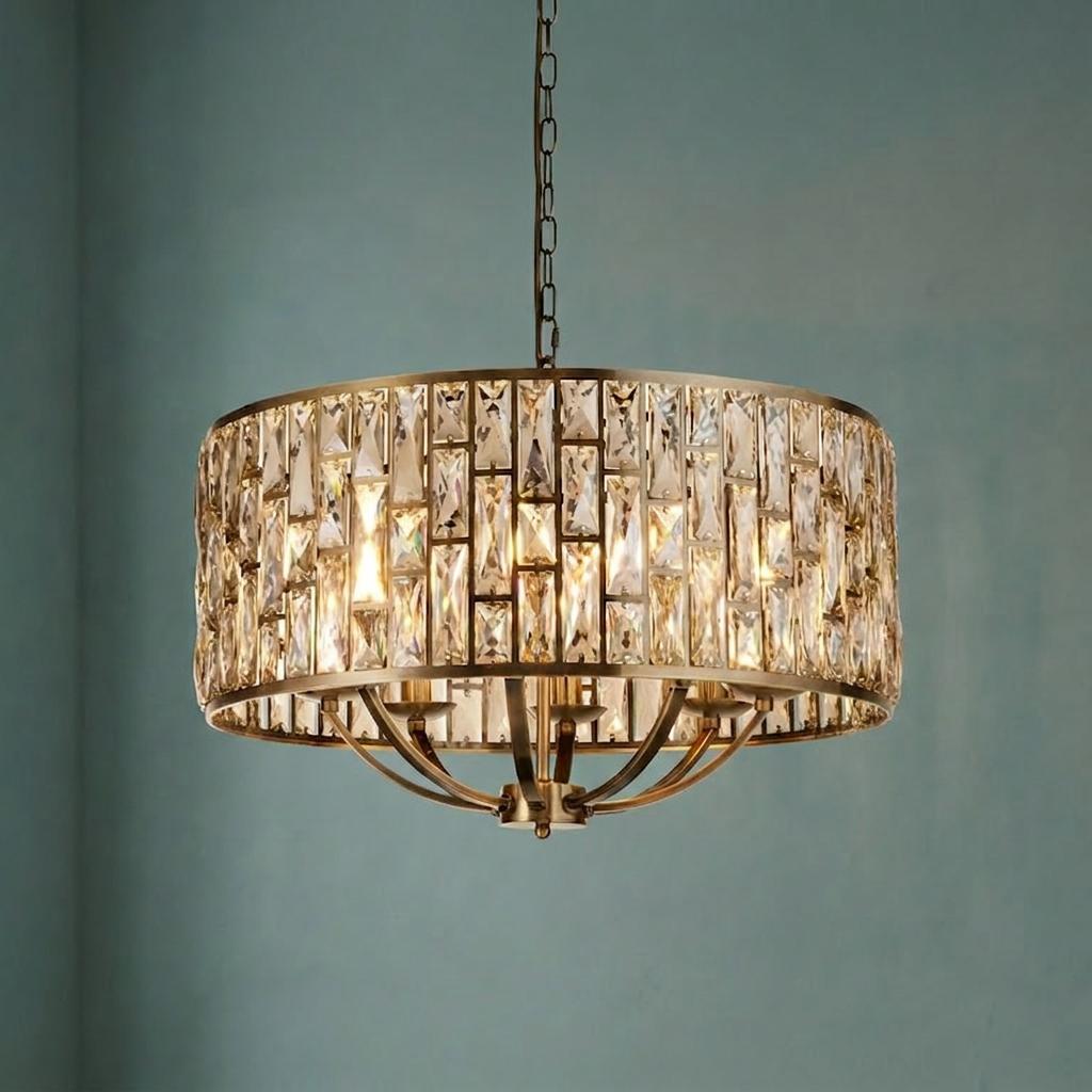 A brass drum-shaped pendant light with champagne glass crystals against a teal background.