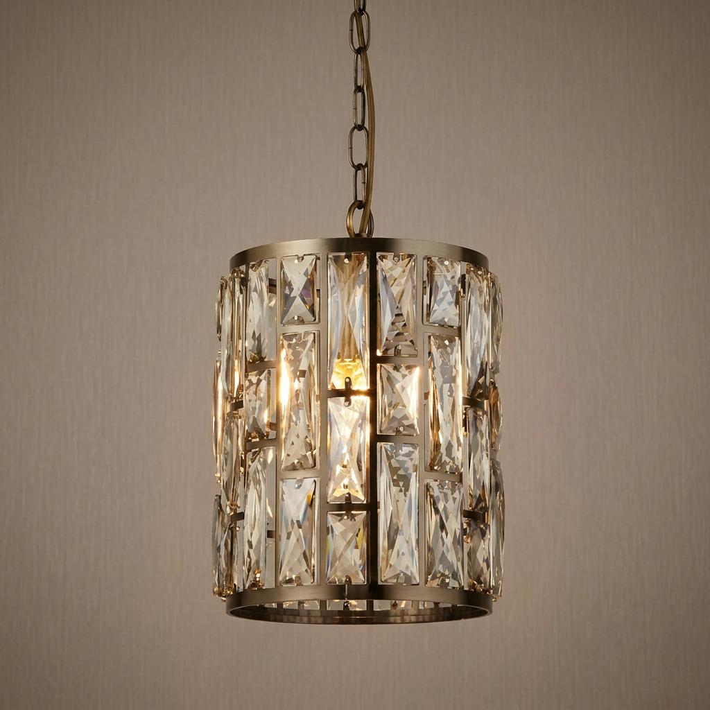 Illuminated cylindrical brass pendant light featuring rectangular champagne glass crystals against a neutral wall.