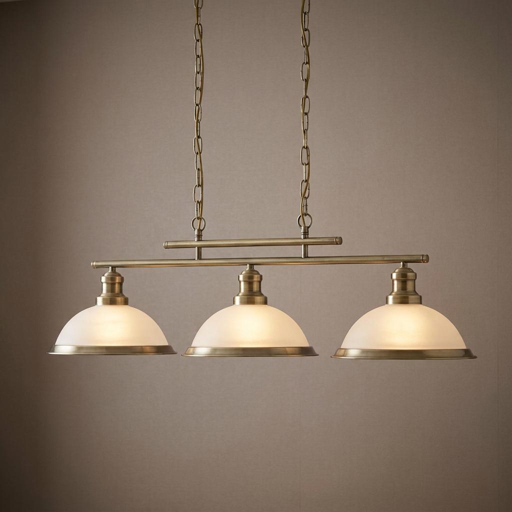 A brass three-light bar pendant ceiling fixture with white frosted glass dome shades, illuminated against a neutral wall.