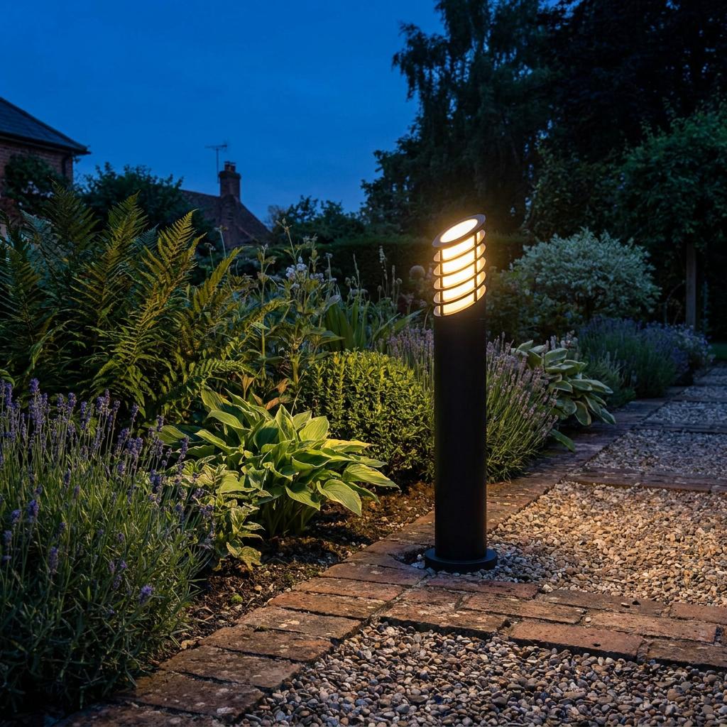 A black Searchlight outdoor bollard light with a warm glow illuminating a garden path at twilight.