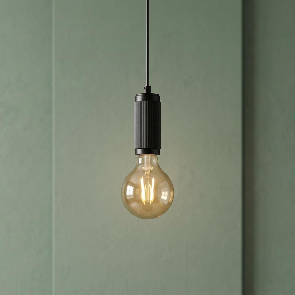 Black pendant light with a textured socket and glowing filament bulb hanging against a sage green paneled wall.