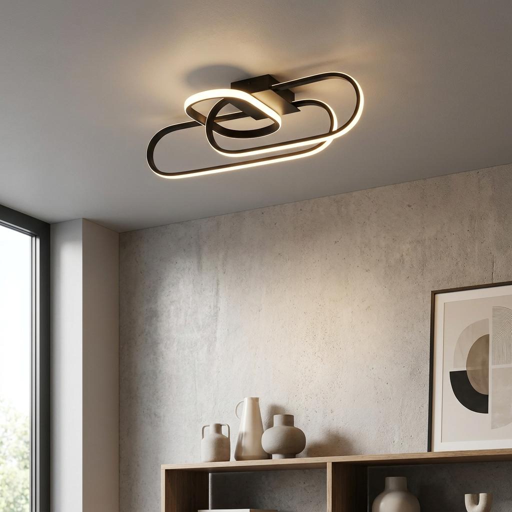 Intertwined black oval LED flush ceiling light mounted on a white ceiling above a modern living space.