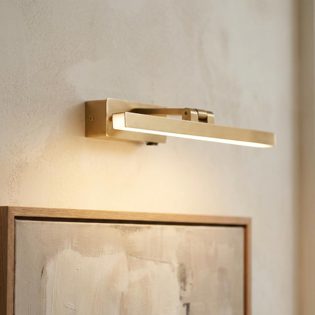 Modern brass LED picture light illuminating an abstract framed painting on a neutral textured wall.