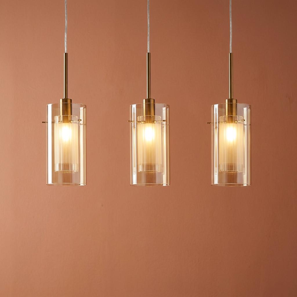 Three bronze bar pendant lights with champagne glass shades and warm light against a terracotta wall.