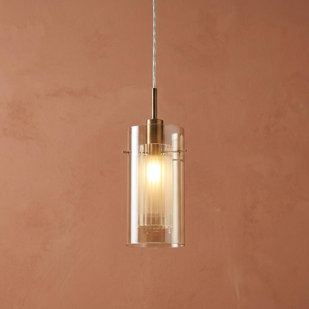 Bronze pendant light with a dual clear and ribbed champagne glass shade glowing against a terracotta wall.