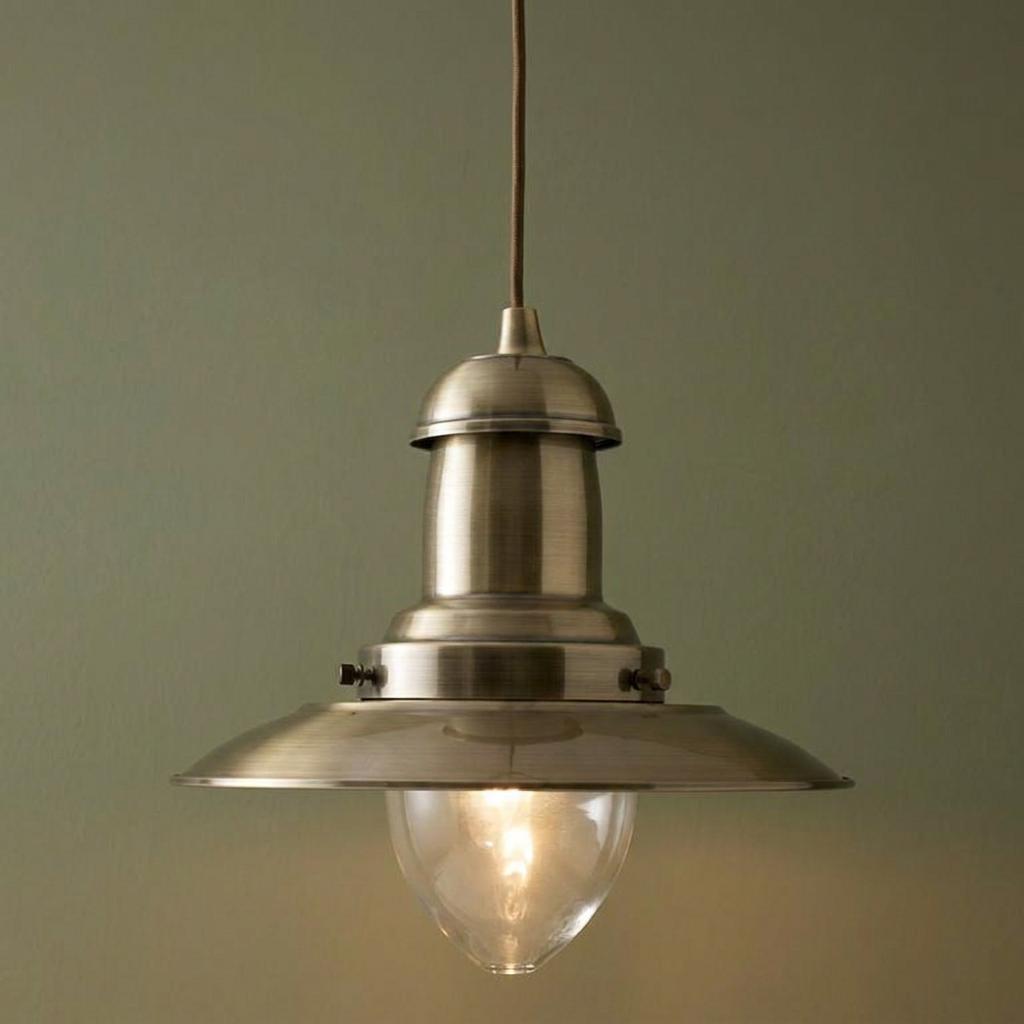 Antique brass fisherman-style pendant light with a clear glass shade lit against a sage green wall.