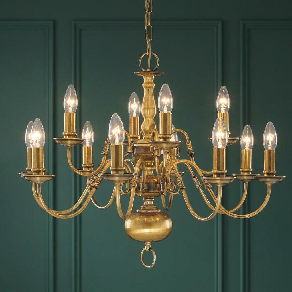 Searchlight Flemish 12 light solid brass chandelier with glowing candle bulbs against a dark green wall.