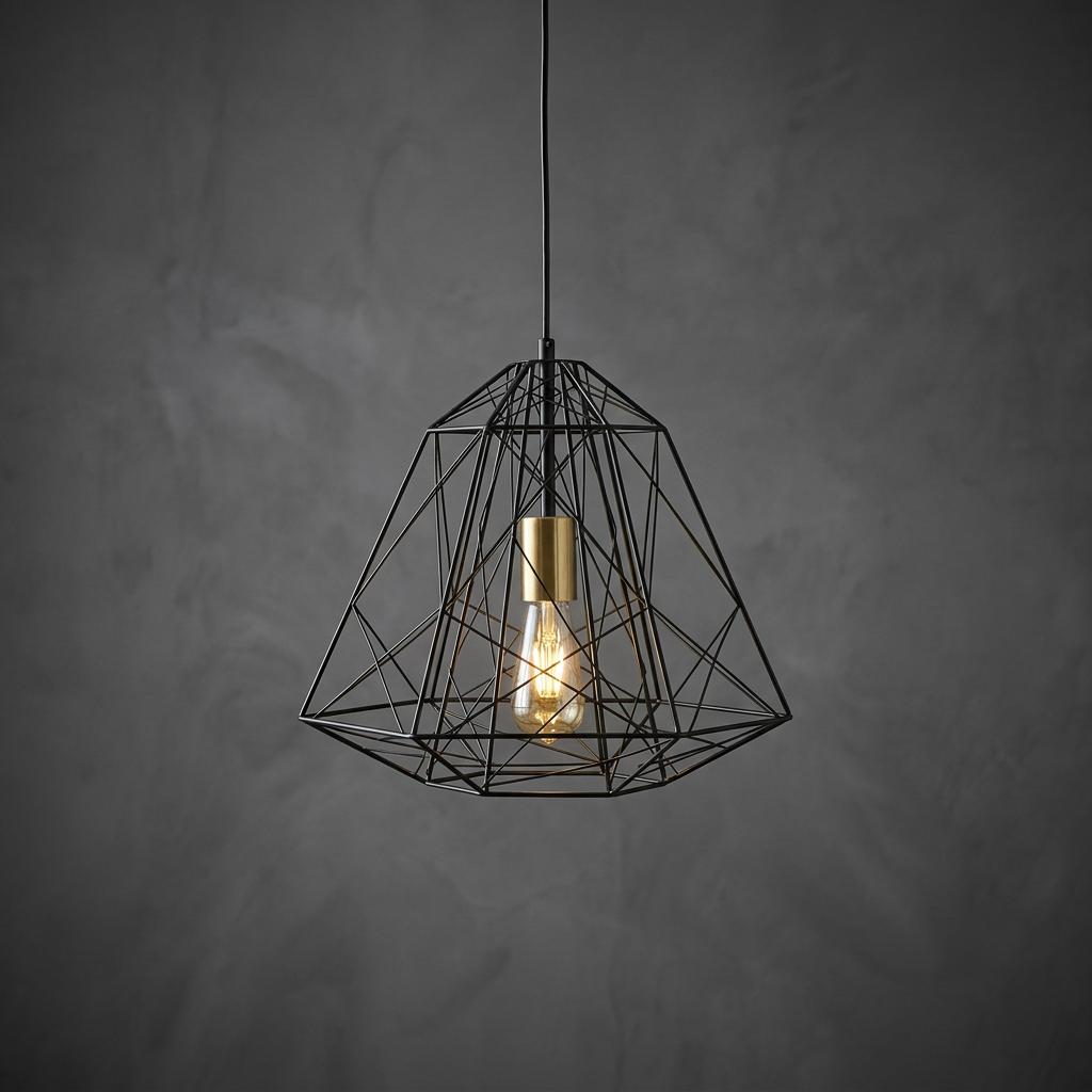 Black geometric wire cage pendant lamp with brass hardware and warm Edison bulb against a grey textured background.