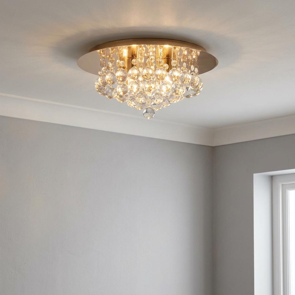 Gold flush mount ceiling light with cascading clear crystal spheres illuminated against a grey wall.